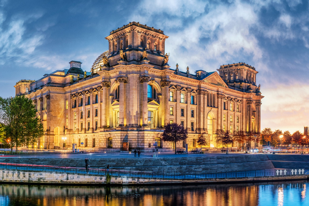 Beleuchtetes Reichstagsgebäude in Berlin bei Abenddämmerung mit Spiegelung im Wasser.