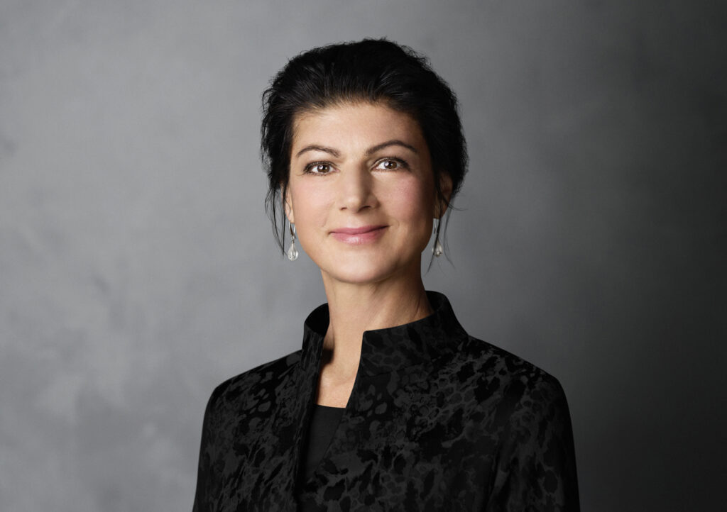 Porträt von Sahra Wagenknecht in einem schwarzen Oberteil vor dunklem Hintergrund.